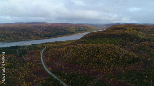 Aerial, tracking, drone shot overlooking the Tenojoki river and the road 970 and the Finland-Norway border, on a,dark rainy, autumn day, near Utsjoki, in Lapland photo