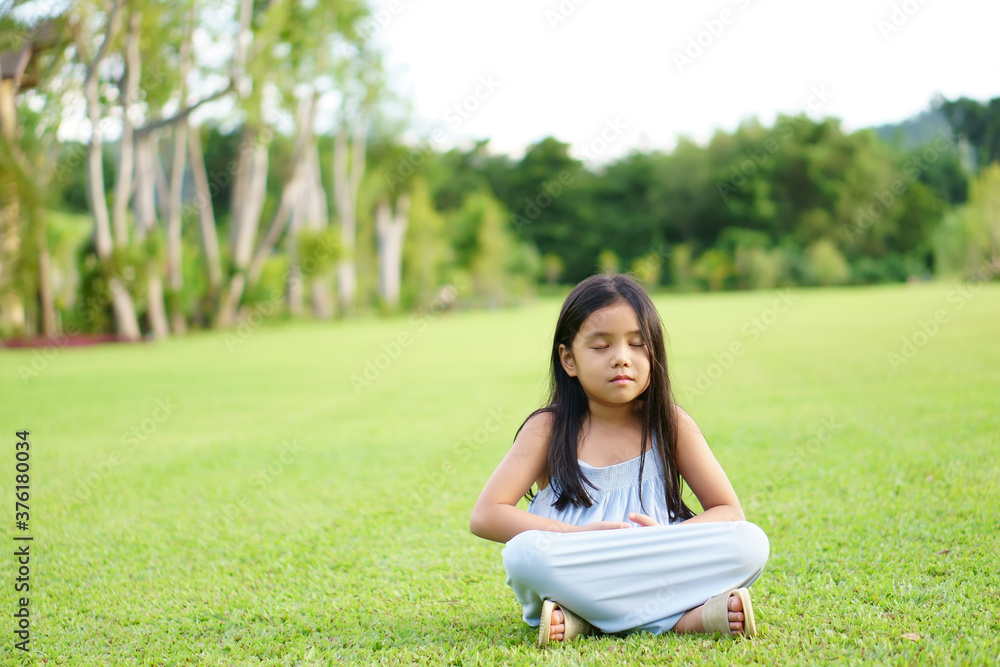 Asian child meditate zen or kid girl smile close eye mind meditating with breath and sit on lawn or meadow grass for peace or yoga relax with hand overlap on tree garden at outdoor temple park to warm Asian child meditate zen or kid girl smile close eye mind meditating with breath and sit on lawn or meadow grass for peace or yoga relax with hand overlap on tree garden at outdoor temple park to warm