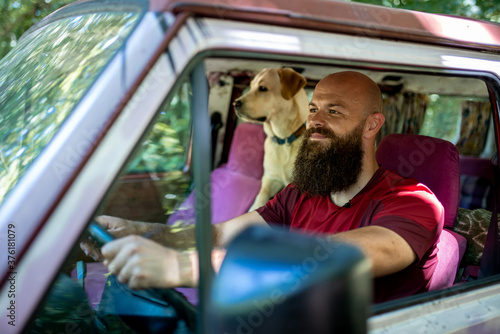 Young bearded man with dog, labrador retriever, traveling together on vintage minivan transport © Drpixel