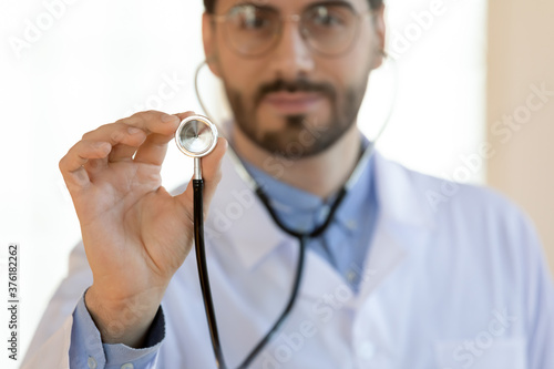 Close up serious young doctor holding stethoscope, medical checkup concept, therapist practitioner gp ready to examine lings or heart sounds with equipment, healthcare and health insurance