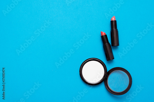 Pair of red lipsticks and white face powder jar on blue flat lay background.