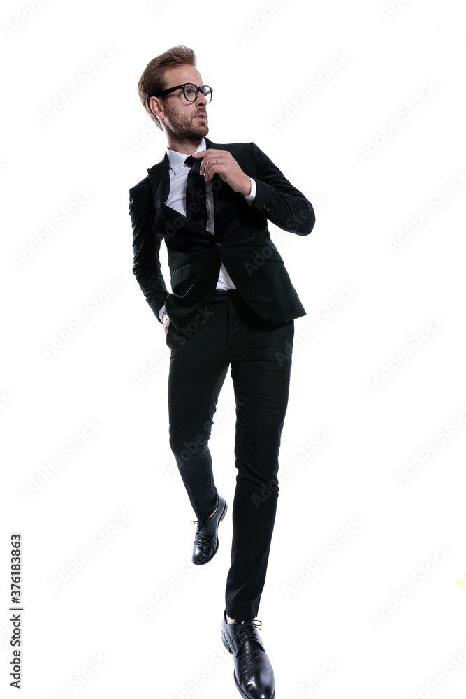 cool stylish man in black suit looking to side and fixing tie cool stylish man in black suit looking to side and fixing tie