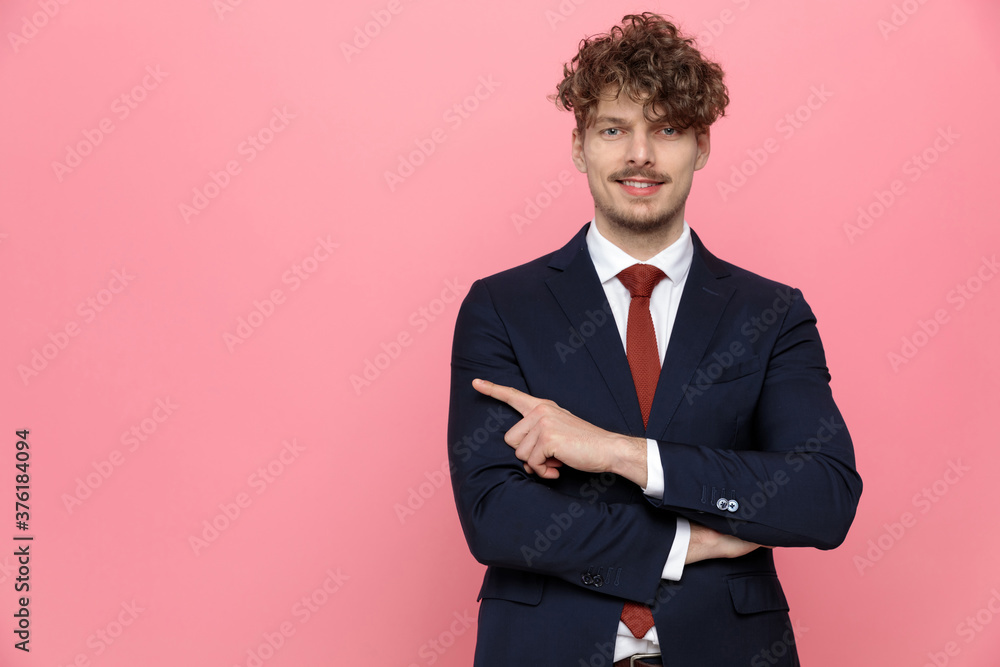 smiling elegant young man in suit pointing finger to side smiling elegant young man in suit pointing finger to side