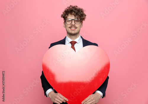 happy young businessman in suit holding big red heart