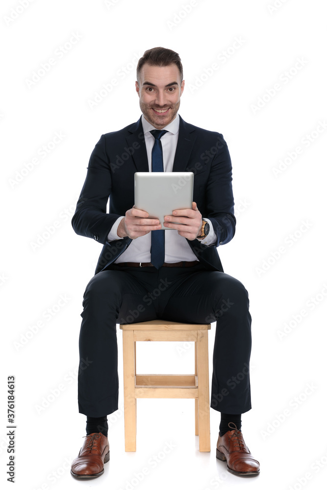 Happy businessman smiling and holding tablet while sitting Happy businessman smiling and holding tablet while sitting