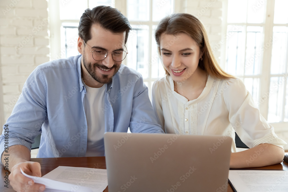 Smiling man and woman using laptop, looking at screen, colleagues or students working on project together, teamwork concept, young couple checking documents, finances, reading good news Smiling man and woman using laptop, looking at screen, colleagues or students working on project together, teamwork concept, young couple checking documents, finances, reading good news