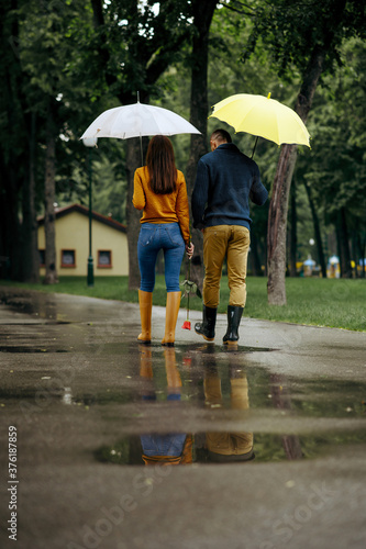 Love couple with umbrellas walks in park, back view