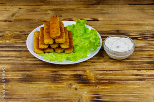 Fried fish fingers on a plate with lettuce and tartar sauce on wooden table