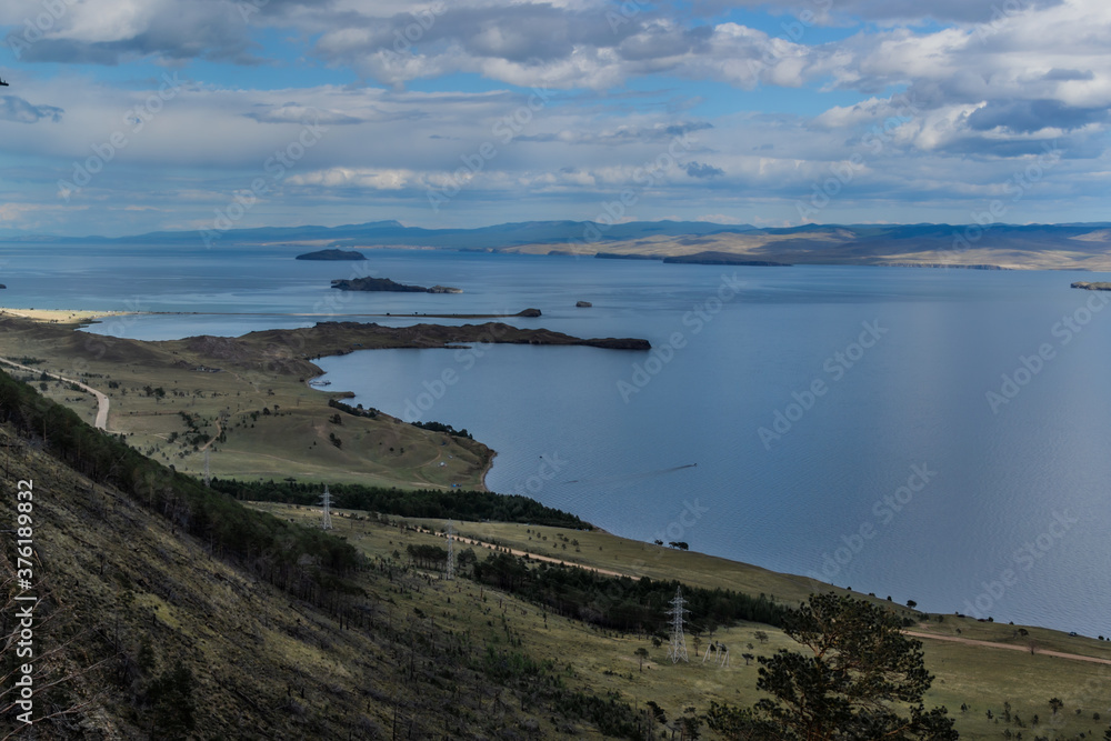 top view of the bay of blue lake Baikal with islands, peninsulas, mountains and hills with green trees, road below