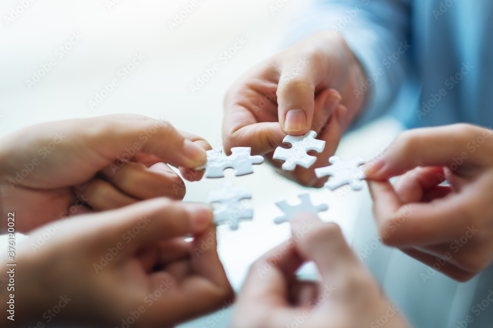 Closeup image of a group of people holding and putting a piece of white jigsaw puzzle together Closeup image of a group of people holding and putting a piece of white jigsaw puzzle together