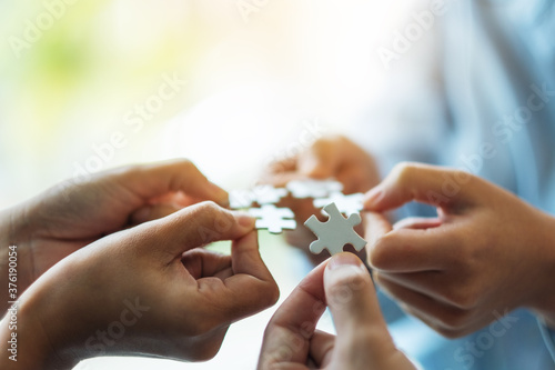 Closeup image of a group of people holding and putting a piece of white jigsaw puzzle together