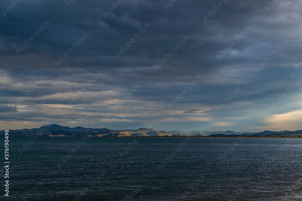 view of the clear calm undulating dark blue water of Lake Baikal, mountains on the horizon, sunset clouds