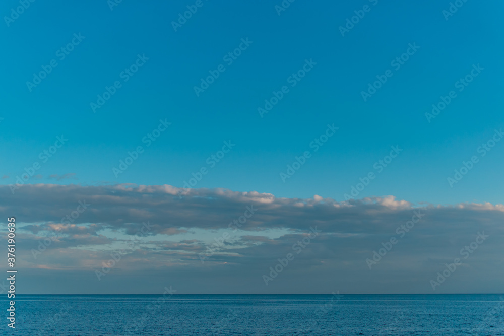 view of the clear calm undulating water of Lake Baikal, sunset clouds on the horizon, blue sky background