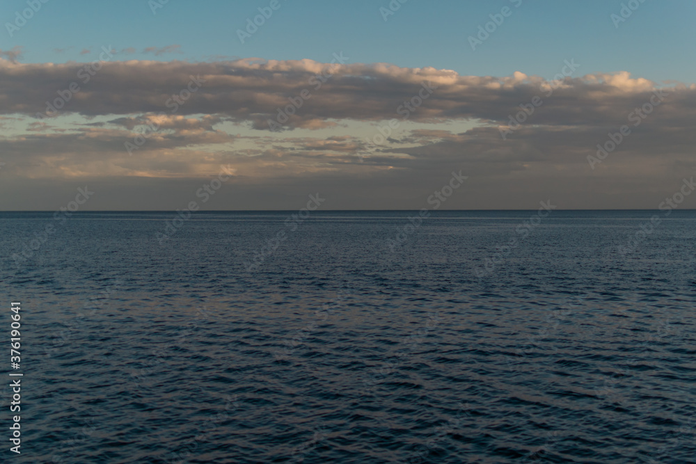 view of the clear calm undulating .ripples water of Lake Baikal, sunset clouds on the horizon, blue sky background