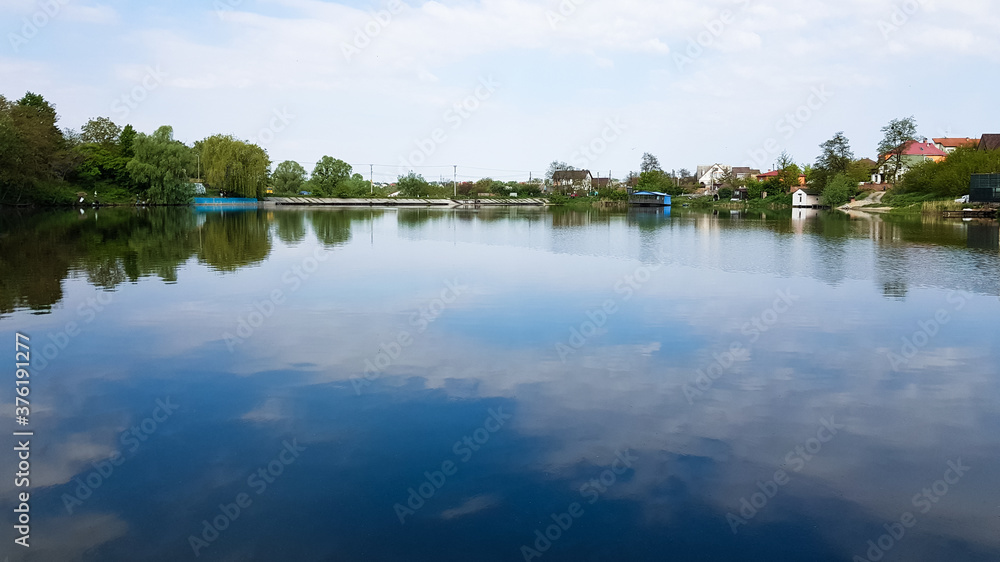Cumulus clouds and sky are reflected in the lake water on a sunny summer day. Beautiful natural landscape.