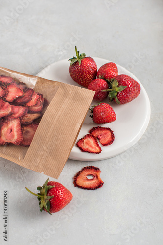 Ripe fresh strawberries and dry strawberry slices fruit chips on a white plate. Copy space, healthy food detoxification concept