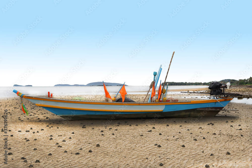 selective focus, a fisherman boat with flags and engine parking on the beach with blue sky in the background