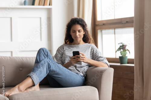 Carefree lazy woman relax on couch in living room hold smart phone use apps  send sms to friend  arrange meeting by message  play new game. Modern tech every day usage  overuse and dependence concept