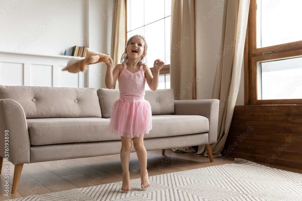 Cute well-dressed girl wear tiara pink fluffy dress hold stuffed animal toy jumps play in living room, listen favourite song feels excited moving have fun. Playtime carefree child, dance hobby concept Cute well-dressed girl wear tiara pink fluffy dress hold stuffed animal toy jumps play in living room, listen favourite song feels excited moving have fun. Playtime carefree child, dance hobby concept