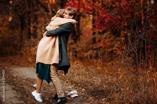happy  couple in love hugs and smiles on the street  autumn  green scarf and cap  beige coat. man and woman on a date  valentines day. walk in the park under an umbrella in the rays of the setting sun