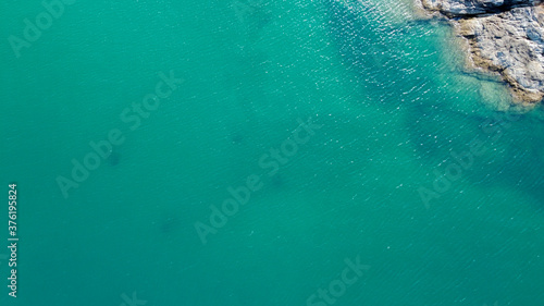 Aerial view. Top view of the turquoise clean sea water. In the upper right corner there is a piece of rock that is washed by the sea. Thailand, Phuket
