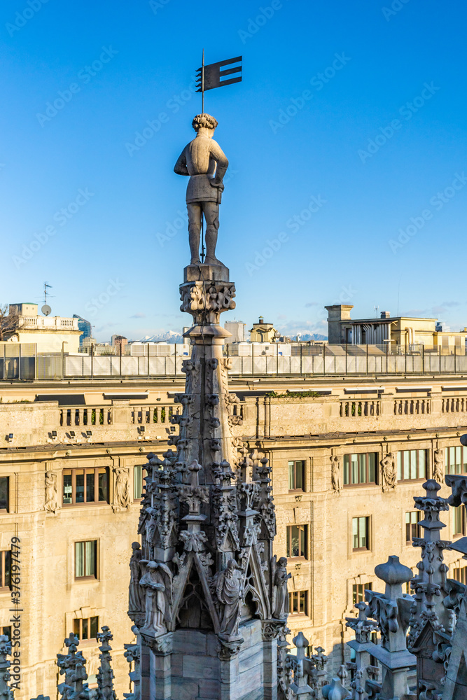 Male statue standing on top of a tower of Duomo cathedral, the famous church in Milan, Italy