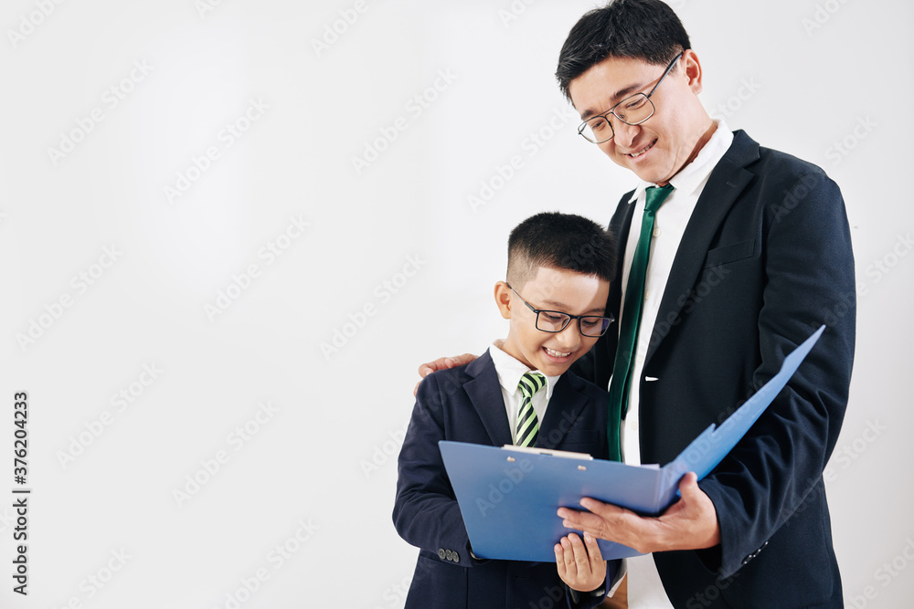 Smiling proud Vietnamese man in suit showing document in folder to his preteen son Smiling proud Vietnamese man in suit showing document in folder to his preteen son