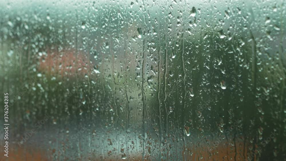 Rain drops sliding slow on window glass in rainy day, de-focused city in background,medium closeup shot Rain drops sliding slow on window glass in rainy day, de-focused city in background,medium closeup shot