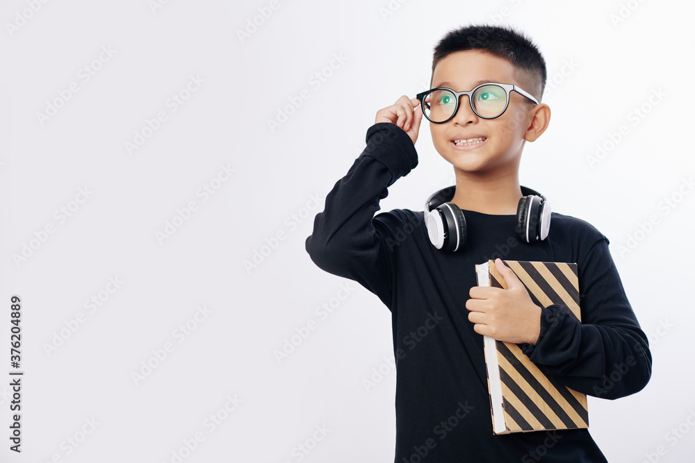 Smart talented Vietnamese kid with book adjusting glasses and looking away Smart talented Vietnamese kid with book adjusting glasses and looking away