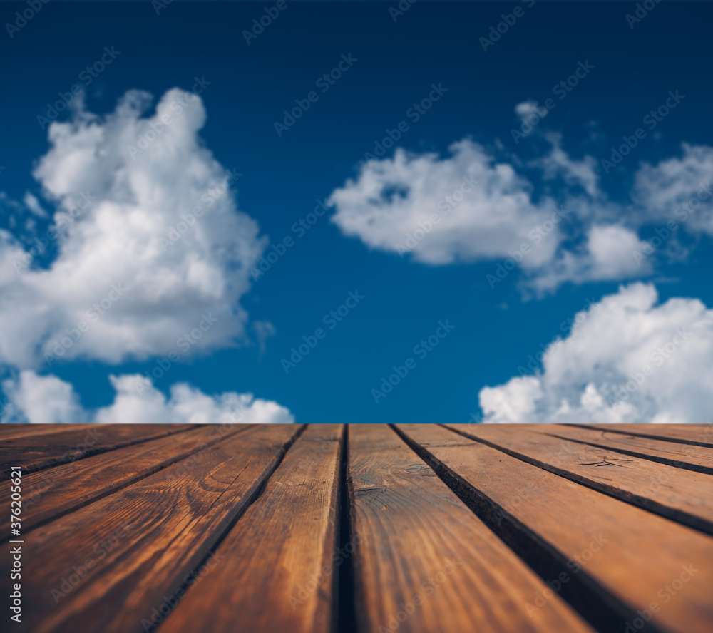 Wooden floor against blue sky with fluffy clouds. 