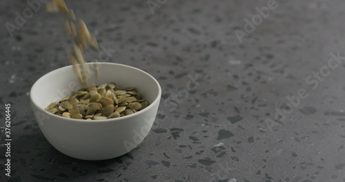 dried pumpkin seeds falling into white bowl on terrazzo countertop