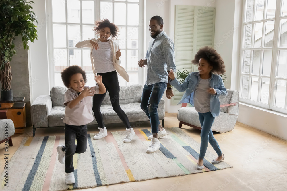 Full length overjoyed african ethnicity family having fun in living room, celebrating freedom. Happy mixed race young couple parents dancing to music with energetic funny biracial children siblings. Full length overjoyed african ethnicity family having fun in living room, celebrating freedom. Happy mixed race young couple parents dancing to music with energetic funny biracial children siblings.