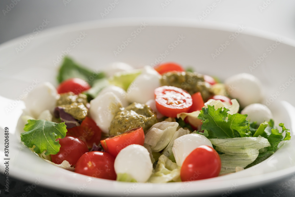 Salad with miced greens , tomatoes and mozzarella in white bowl