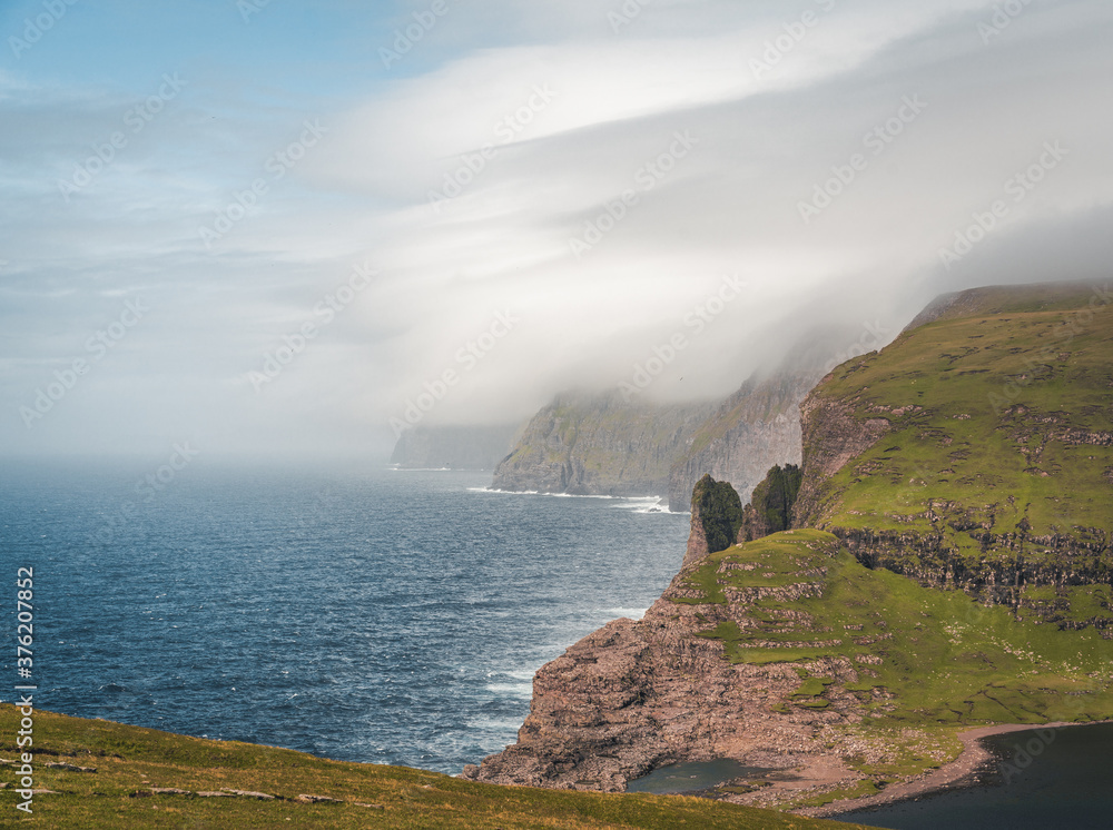 Faroe Islands Traelanipa the slaves rock cliff is seen rising over the ocean next to lake Sorvagsvatn. Clouds and blue sky during suommer on the island vagar in the Faroe Islands.