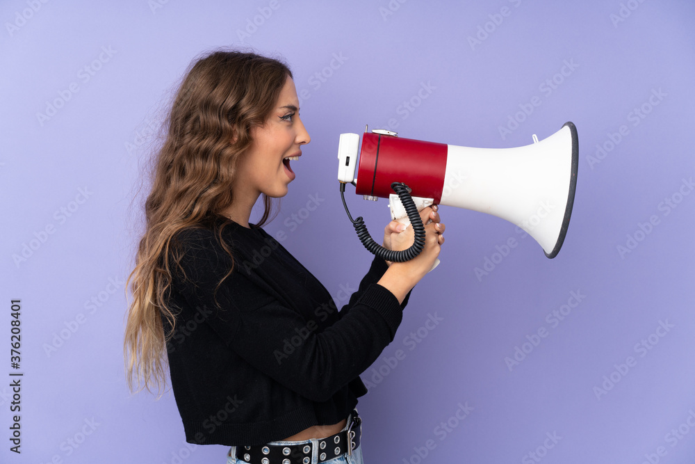 Young woman over isolated purple background shouting through a megaphone Young woman over isolated purple background shouting through a megaphone