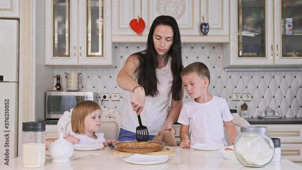 Family of mother and two kids cutting raspberry pie in kitchen. Pretty mother with little son and daughter cooking cake at home. 4K, UHD Family of mother and two kids cutting raspberry pie in kitchen. Pretty mother with little son and daughter cooking cake at home. 4K, UHD
