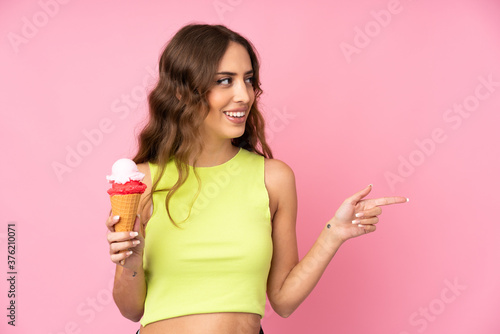 Young woman holding a cornet ice cream over isolated on a pink background pointing to the side to present a product