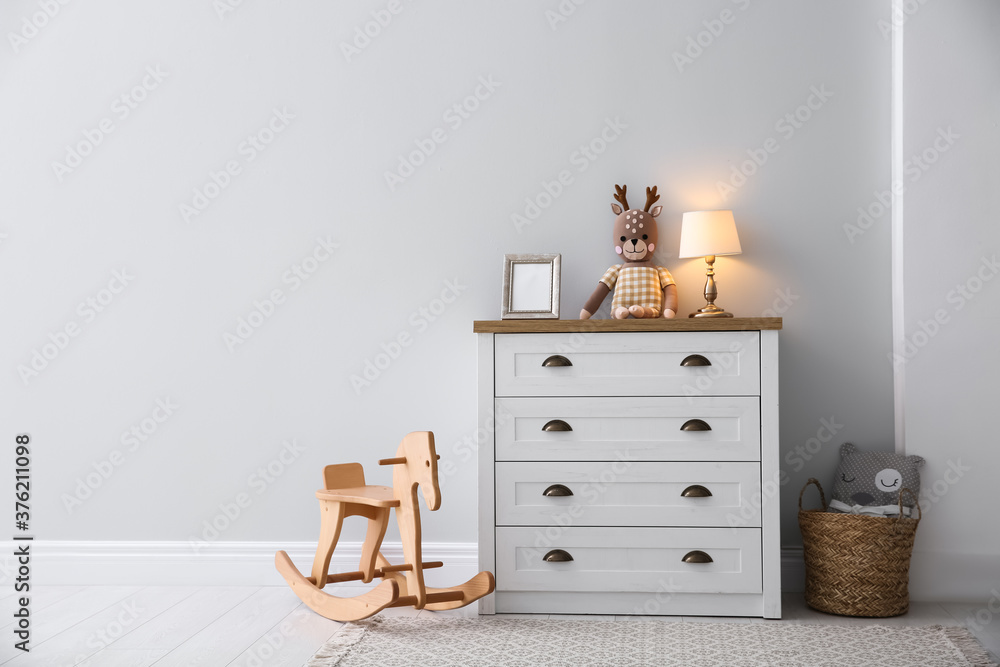Fototapeta premium Modern white chest of drawers near light wall in child room, space for text. Interior design