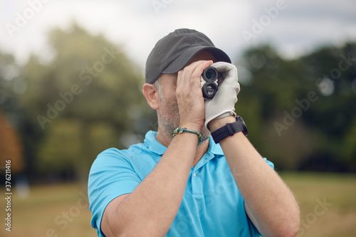 Golfer using a rangefinder to measure the distance to the hole holding it to his eye as he peers down the fairway in a close up head and shoulders for a healthy active lifestyle or sport concept photo