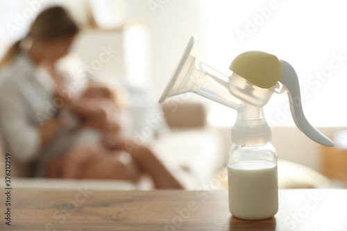 Mother feeding her little baby at home, focus on breast pump with milk. Healthy growth