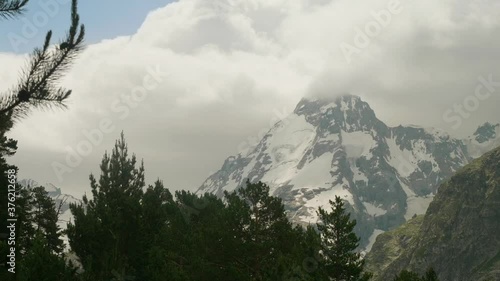 View of bare mountains with peaks covered with snow and with white fluffy clouds above photo