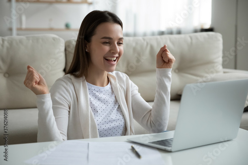 Emotional happy young woman looking at laptop screen, celebrating banking good news notification. Euphoric millennial lady feeling excited about online lottery win notification, good luck concept.