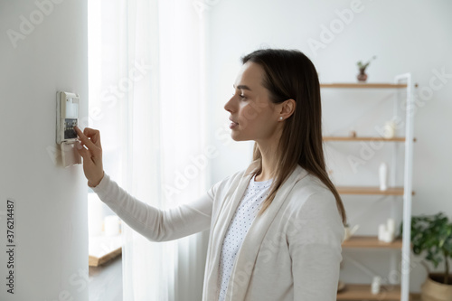 Side view pleasant young woman using smart home system or activating modern alarm system before leaving apartment. Happy lady turning off easy security technology, when returning house or flat. photo