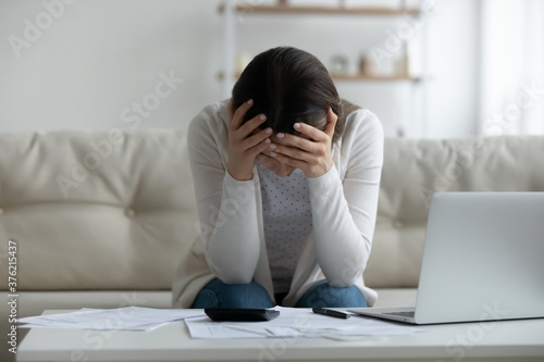 Frustrated young woman holding head in hands, feeling stressed about financial problems. Unhappy millennial girl having troubles with managing budget, termination banking letter, bankruptcy concept.