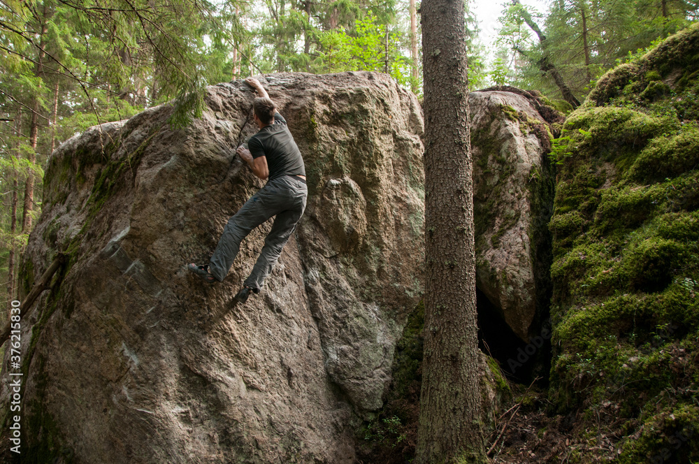 Man climbing a bouldering problem on a rock covered with green moss. Bouldering in a magic wood. Climber in a black short. Outdoor climbing. Man climbing a bouldering problem on a rock covered with green moss. Bouldering in a magic wood. Climber in a black short. Outdoor climbing.