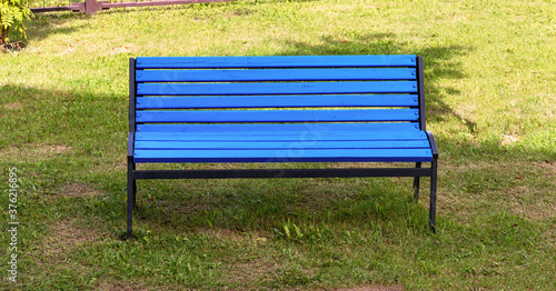 lonely wooden blue bench stands on green grass of public town park