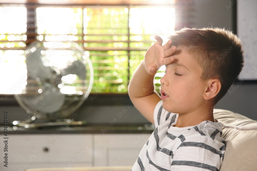 Little boy suffering from heat near fan at home. Summer season Little boy suffering from heat near fan at home. Summer season