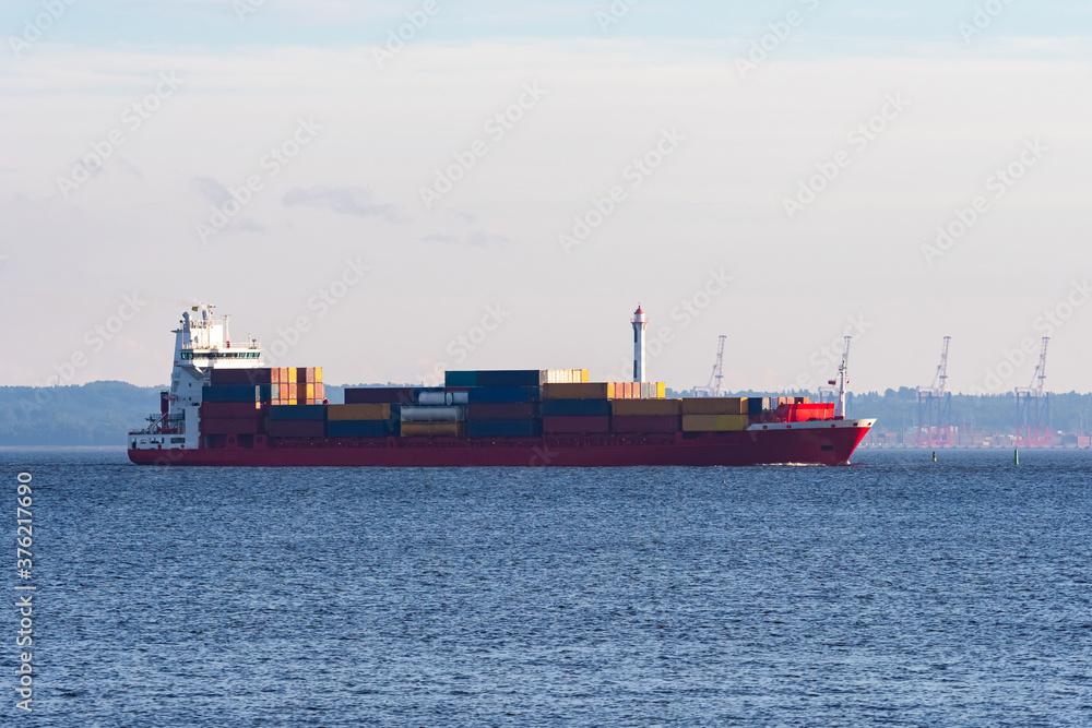 Sea cargo ship sails to open sea. Sea container ship on summer day. Vessel for transport of containers is sailing to port. Transportation goods using container ship. Many containers loaded on vessel