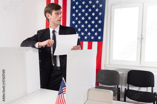 USA voter in presidential election. Man at polling station. USA flag next to American. Concept - person participates in voting in elections. Voting in presidential elections. Man in voting booth