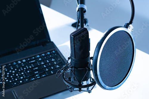 Microphone next to a laptop. Sound recording equipment. Concept - working musto radio host. Equipment for a radio host. Foam pop filter in front of microphone. Sound recording services. photo